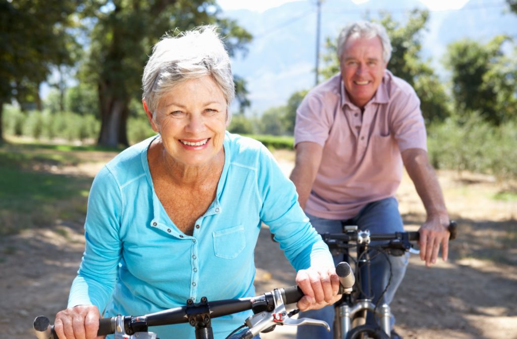 2 older adults smiling and riding a bike in a park