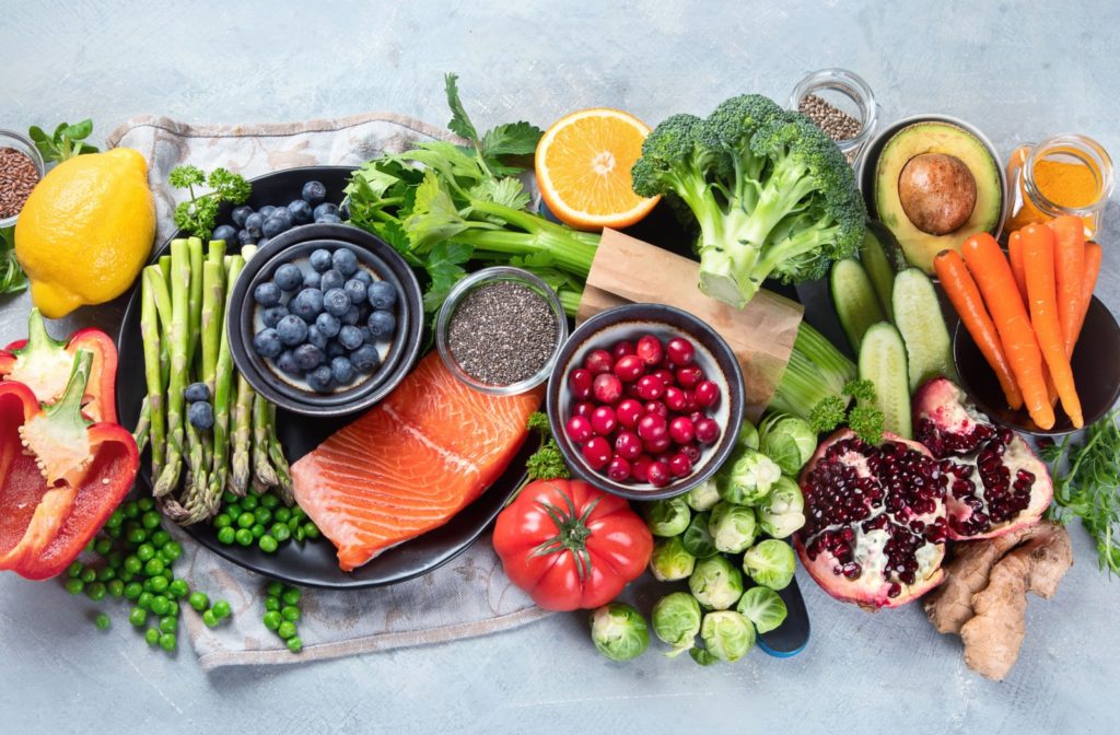 A spread of heart-healthy fruits, vegetables, and fish on a gray background.